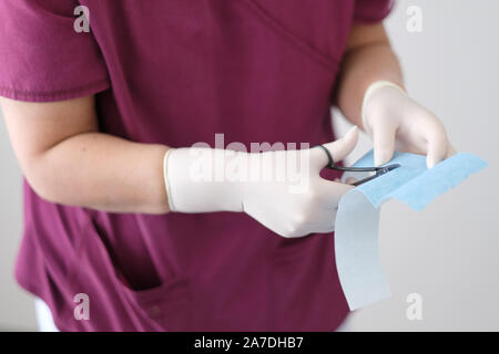 Eine Krankenschwester in Gummi Schutzhandschuhe schneidet ein Stück op-Putz mit Schere Stockfoto