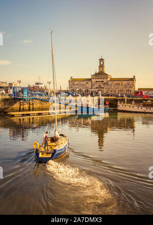 Yacht segeln zu seinen Liegeplatz in Ramsgate Royal Harbour, die denkmalgeschützten Gebäude der Uhr Haus und Turm im Hintergrund werden Siehe spiegeln Stockfoto