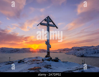 Orthodoxes Kreuz auf der Spitze des schneebedeckten Berg bei Sonnenaufgang. Barentssee Küste bei Sonnenaufgang. Teriberka, Region Murmansk, Kola Halbinsel. Russland Stockfoto