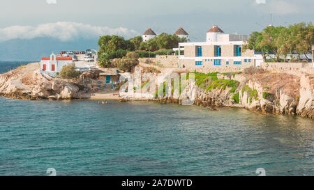 Blick auf die weißen Gebäuden und berühmten Windmühlen am Meer in Mykonos mit Touristen schwimmen Stockfoto