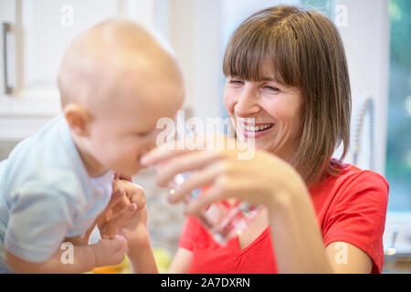 Das Konzept der Mutterschaft, Nanny, Kindheit und Kindheit. Innen- schuss in der Küche. Zwei Frauen und ein Kind in ihren Armen, das Kind Wasser gegeben wird, ein Stockfoto