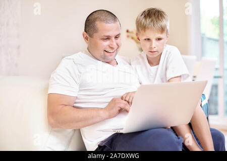 Der Sohn und sein Vater auf der Couch sitzen, an einem Laptop suchen, gerne Emotionen aus, was er sah, eine glückliche Familie. Stockfoto