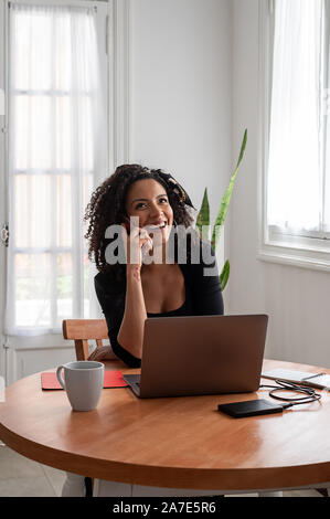 Schuss der jungen Latin Frau zu Hause mit Laptop und Unterlagen arbeiten Stockfoto