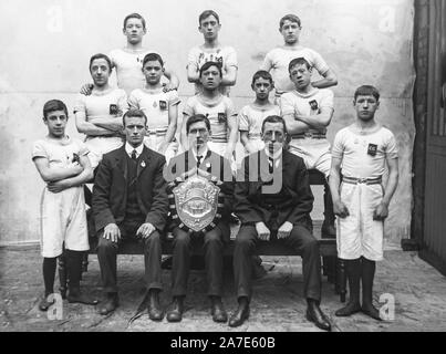 Ein Vintage späten viktorianischen early Edwardian schwarz-weiß Foto zeigt eine Gruppe von jungen englischen Jungen Turnerinnen und Turner für eine Kamera während ihr Trainer oder Manager zeigt eine große Trophäe Schild posieren. Stockfoto
