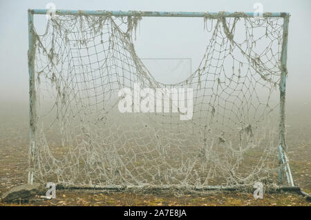 Alte, leere verlassene Fußballplatz und Tor mit einem verworrenen Netz in einem leichten Nebel Stockfoto