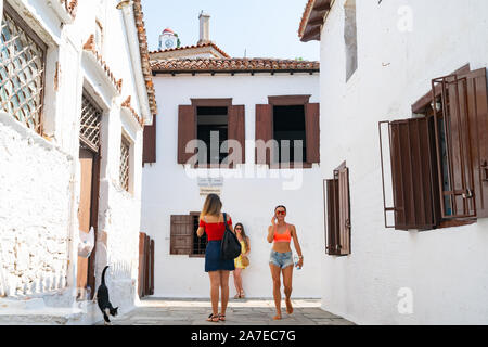 Skiathos Griechenland - 31. Juli 2019; drei Frauen und schwarze Katze in der Gasse durch die typisch griechische Insel Gebäude mit Rollläden und Fenstern umgeben Stockfoto
