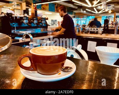 Eine Tasse frisch zubereiteten Cappuccino mit Dekoration mit der Barista im Hintergrund und unscharf Stockfoto