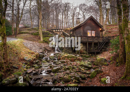 Kleine Wassermühle in einem Bach im Winter ohne Blätter, von Wald umgeben. Wenig Wasser im Bach. Stockfoto