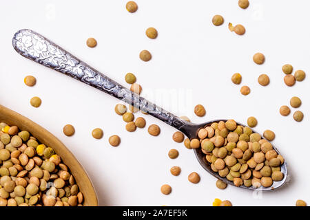 Linsen in der dekorativen Metalllöffel mit zufälligen verstreuten Samen auf weißem Hintergrund. Stockfoto