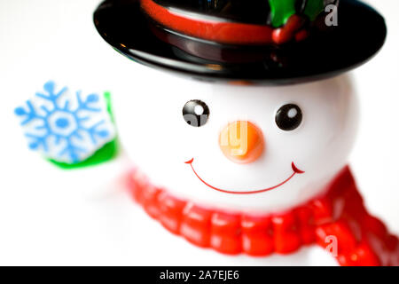 Nahaufnahme von adorable Glas Figur Schneemann trägt einen Schal und Hut einen blauen Schneeflocke Stockfoto