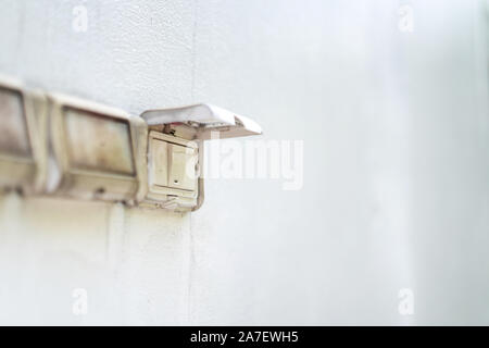 Schließen Sie die elektrischen Schalter mit der Abdeckung auf es Outdoor regen oder Sonnenlicht zu schützen. Es Stick auf dem Zement weiße Wand. Stockfoto