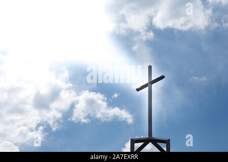 Ein christliches Kruzifix auf einer Kirche, die von Lichtstrahlen von oben umragt wird. Stockfoto