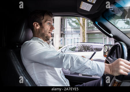 Ein Kaukasischer im mittleren Alter lenkte das Fahren ab, während er ein mobiles Gerät benutzte, stoppt sein Fahrzeug plötzlich, um einen Unfall zu vermeiden. Stockfoto