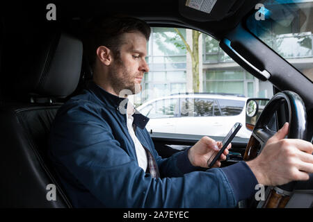 Ein Kaukasischer im mittleren Alter lenkte das Fahren ab, während er ein mobiles Gerät benutzte. Stockfoto