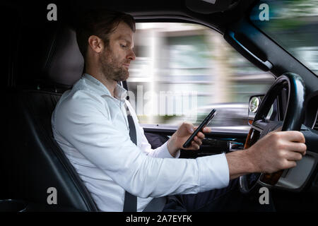Ein Kaukasischer im mittleren Alter lenkte das Fahren ab, während er ein mobiles Gerät benutzte. Stockfoto