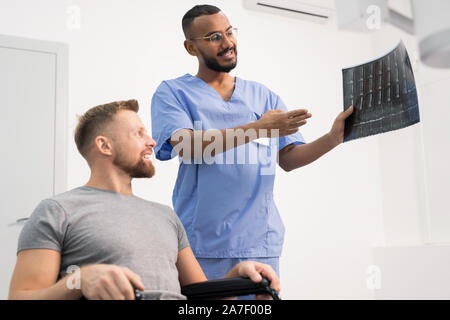 Radiologe in Uniform zeigen Patienten im Rollstuhl x-ray von seinem gebrochenen Gemeinsame Stockfoto
