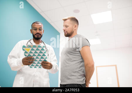 Junger Arzt in Jungtieren auf medizinische Dokument mit Patienten in der Nähe von Stockfoto