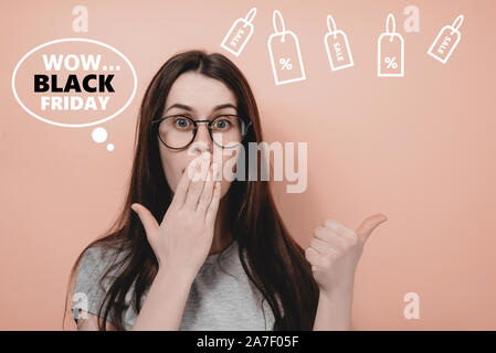 Junge weibliche in Brillen deckt Mund mit Palm, zieht ihre Aufmerksamkeit bei copy Platz, steht gegen die rosa Wand. Die menschlichen Gefühle, schwarz fr Stockfoto