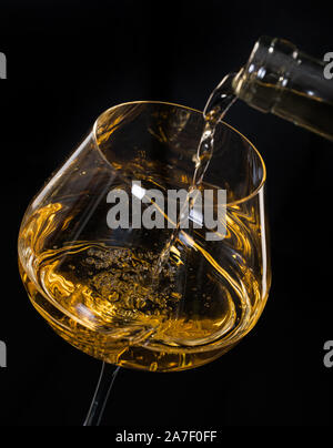 Weißer Wein Ausgießen aus der Flasche in ein Weinglas auf schwarzem Hintergrund Stockfoto