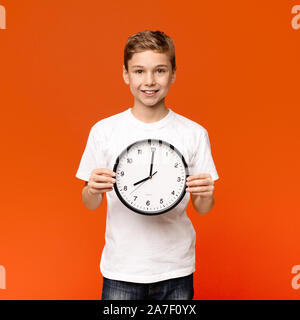 Lächelnd teen boy Holding grosse Uhr, orange Hintergrund Stockfoto