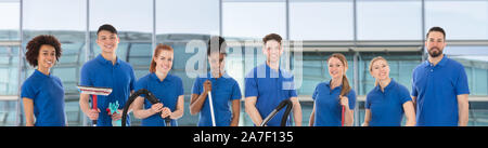 Porträt eines lächelnden Diverse Jungen Hausmeister mit der Reinigung der Geräte gegen Fenster Glas Stockfoto