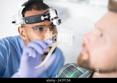 Junger Arzt in Handschuhen und einheitliche, kranken Ohr des Patienten zu prüfen. Stockfoto