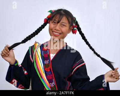 Lächelnde thailändische Akha Mädchen trägt eine traditionelle Akha Tracht und zieht ihre langen Zöpfen. Stockfoto