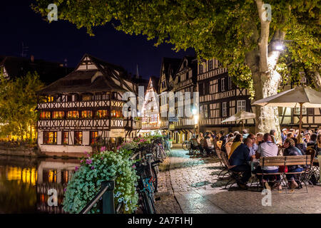 Die Menschen genießen ein Straßencafe in der Nacht auf dem Kanal unter den Bäumen des Benjamin Zix Quadrat in der Petite France Viertels in Straßburg, Frankreich. Stockfoto