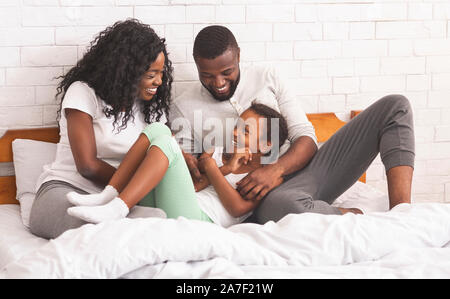 Schwarze Eltern kitzeln ihre Tochter, während zusammen im Bett liegend Stockfoto