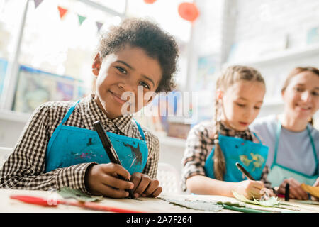 Glückliche Schüler mit textmarker an Sie, während Sie von Schreibtisch bei Lektion sitzen Stockfoto