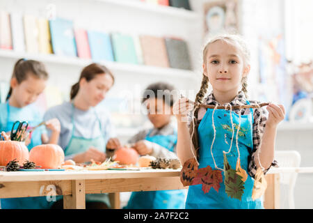 Hübsche Blondine Schulmädchen holding Stick mit mehreren halloween Blätter auf Threads Stockfoto