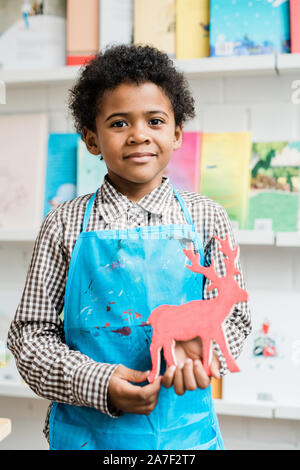 Gerne afrikanische Schüler in der blauen Schürze Holding handmade Deer Stockfoto