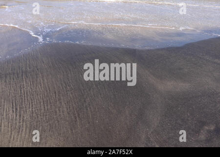 Feiner weisser Sandstrand, gestromt mit schwarzen vulkanischen Sand auf der Insel Bali. Ein interessanter Effekt von Meer, Wellen, Brandung und Mischen von Sands erstellt Stockfoto