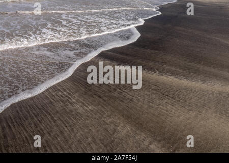 Feiner weisser Sandstrand, gestromt mit schwarzen vulkanischen Sand auf der Insel Bali. Ein interessanter Effekt von Meer, Wellen, Brandung und Mischen von Sands erstellt Stockfoto