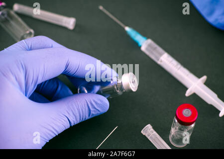 Person Hände in medizinische Handschuhe mit Impfstoff Durchstechflasche. Grüner Hintergrund mit Spritzen und Durchstechflaschen. Stockfoto