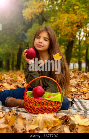 Kleine Mädchen bei einem Picknick im Herbst Park isst ein reifer roter Apfel sitzt auf gefallene Laub Stockfoto