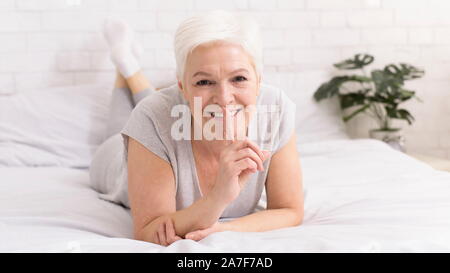 Geheimnisvolle ältere Frau mit den Finger auf den Mund, im Bett liegend Stockfoto