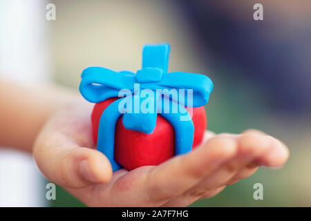 Junge hält Geschenk mit blauer Schleife umwickelt. Geringe Tiefenschärfe. Close Up. Geschenkbox und Band sind aus Lehm gemacht (Knetmasse). Stockfoto