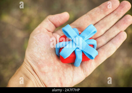 Person, die Geschenk mit blauer Schleife umwickelt. Geringe Tiefenschärfe. Close Up. Geschenkbox und Band sind aus Lehm gemacht (Knetmasse). Stockfoto