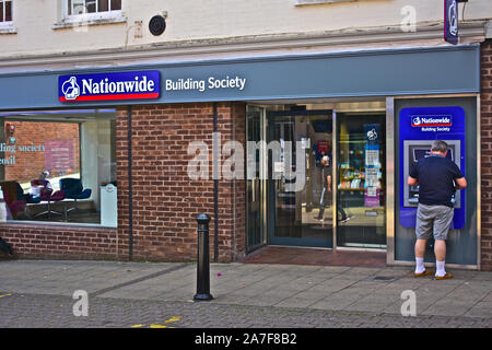 Mann in Shorts erhalten Bargeld vom Geldautomaten außerhalb der Nationwide Building Society Räumlichkeiten in Yeovil Town Center. Stockfoto