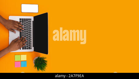 Schwarze Frau Tippen auf Laptop an worplace auf orange Hintergrund Stockfoto