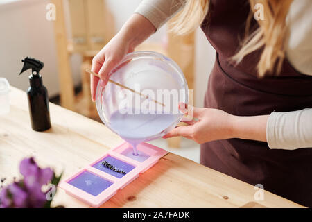 Hände von handwerkerin in Schürze violett flüssige Seife Masse gießen in Silikonformen Stockfoto