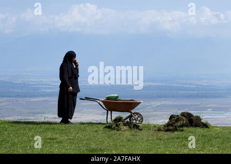 Georgien, 2019: alte Nonne bei der Gartenarbeit erreicht für Mobiltelefon - bodbe Monastery Stockfoto