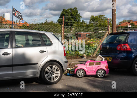 Ein Gedumpten childs Spielzeug Auto sitzt zwischen zwei Limousine Autos auf der Watling Immobilien in Nord London UK Stockfoto