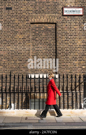 Bild eines rot beschichtet Frau, die ihren Weg entlang Lincoln's Inn Fields, London UK Stockfoto