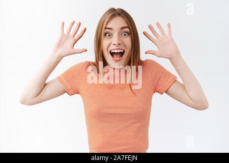 Überrascht , gut aussehende Frau in gestreiften T-Shirt, emotional reagieren auf wunderbare, fantastische Nachrichten, schreien erstaunt, lächelnd und heben die Hände Stockfoto