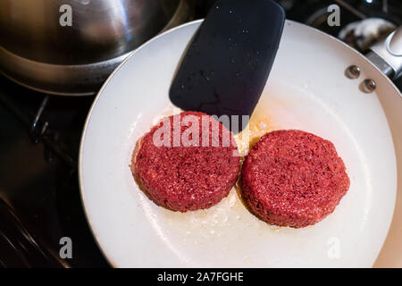 Nahaufnahme von zwei vegan Fleisch würstchenpastete Kochen auf Keramik nonstick Pfanne mit Öl fett Spachtel umdrehen Stockfoto