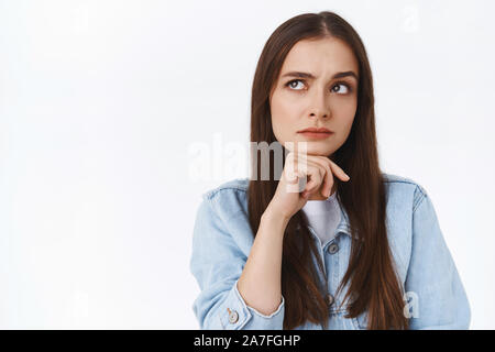 Nachdenklich ernsten und nachdenklichen 20s Girl suchen, berühren, Kinn und Stirn, linke obere Ecke, Denken, mit Blick auf harte Wahl, stehend Stockfoto