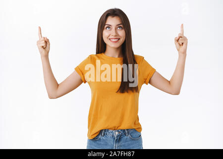 Zufrieden, gut aussehende zarte junge Frau im gelben T-Shirt zeigen Sie die Finger nach oben, lächelte zufrieden amüsiert Ausdruck und interessante Stockfoto