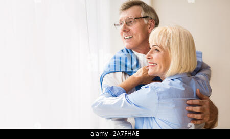 Reifes Paar umarmen und schauen durch das Fenster Stockfoto